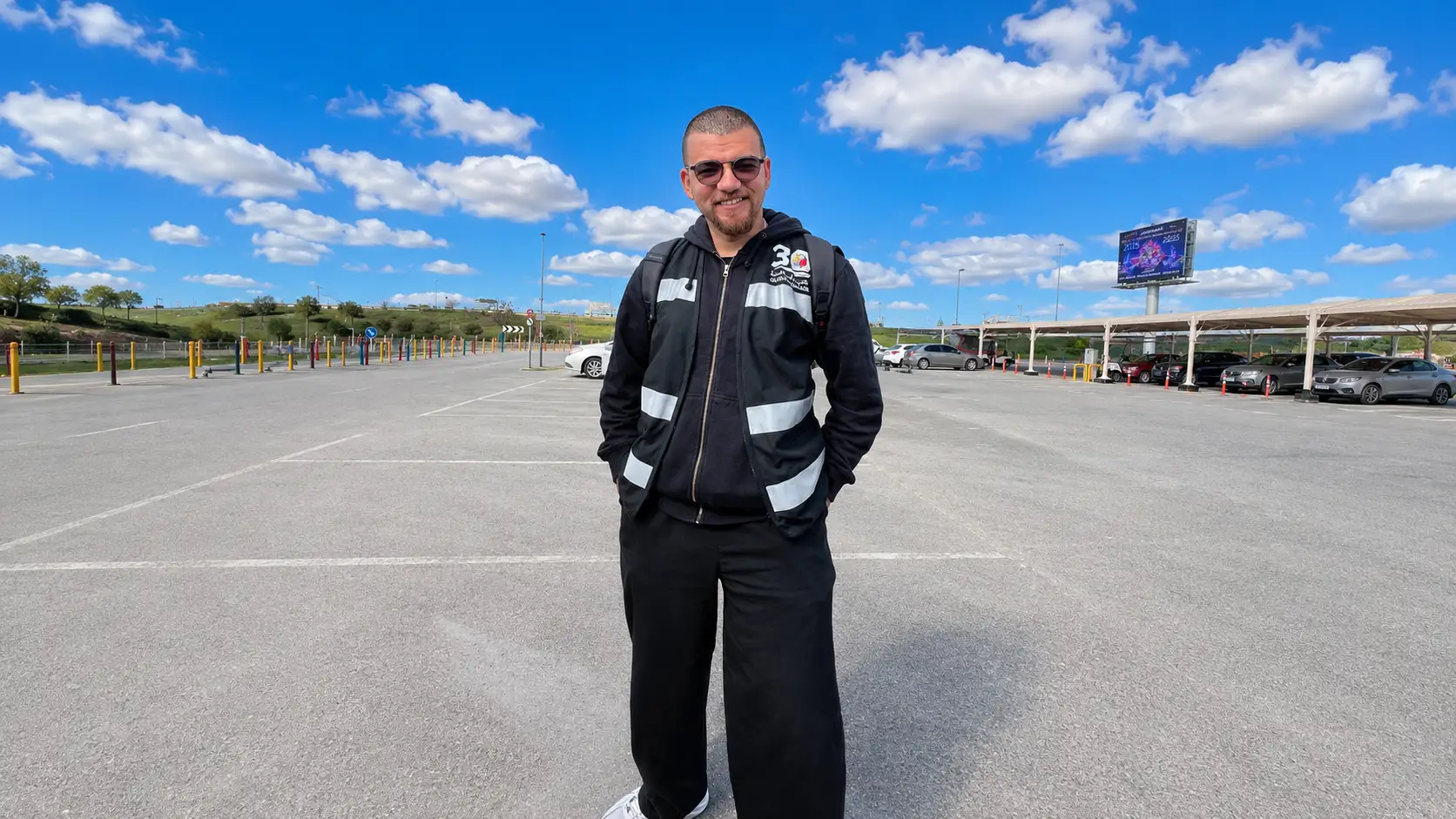 Ahmed Osama standing in an empty Global Village car park, wearing a Season 30 crew jacket.